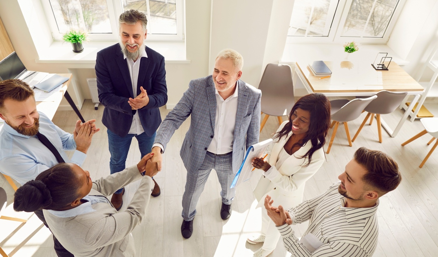 African american women shaking hands with man celebrating success, with a crowd of customers around, signifying customer trust in an office setting.