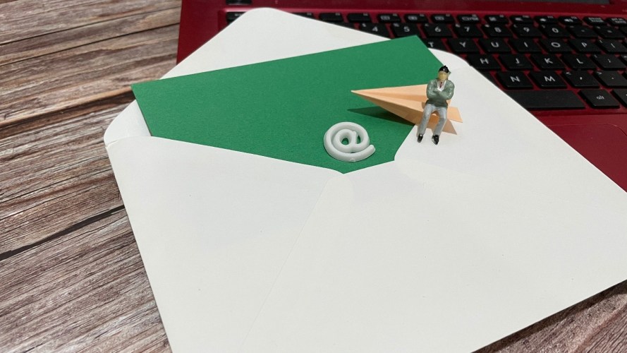 An oversized envelope with ampersand and arrow and SMB owner sitting on top of a desk, symbolizing email marketing.