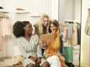 Mixed-races of three pretty young girls friends sitting in clothes store and trying a purse before purchasing.