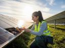 A field service management woman in a yellow safety vest inspects solar panels in a green field on a sunny day