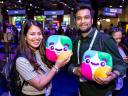 Two attendees at a Salesforce event smile while holding colorful mascot plush toys on a busy expo floor.