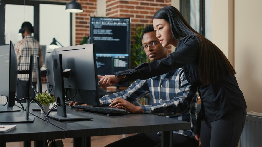 Two colleagues review information on a computer monitor in a modern office.