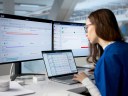 A healthcare manager using a health CRM at a desk with three monitors.