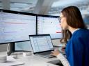 A healthcare manager using a health CRM at a desk with three monitors.