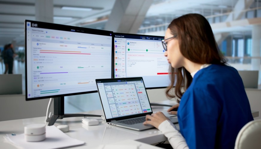 A healthcare manager using a health CRM at a desk with three monitors.
