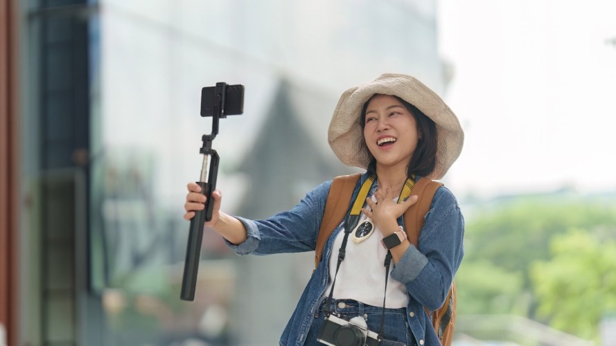 Asian woman vlogging with smartphone on selfie stick for travel content