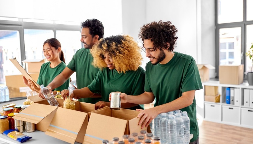 charity, donation and volunteering concept - international group of happy smiling volunteers packing food in boxes