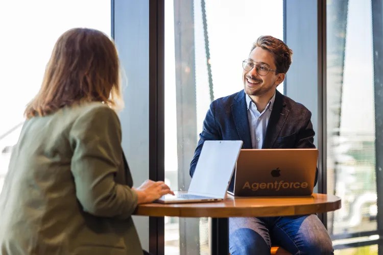 A man and a woman sit at tables with laptops talking