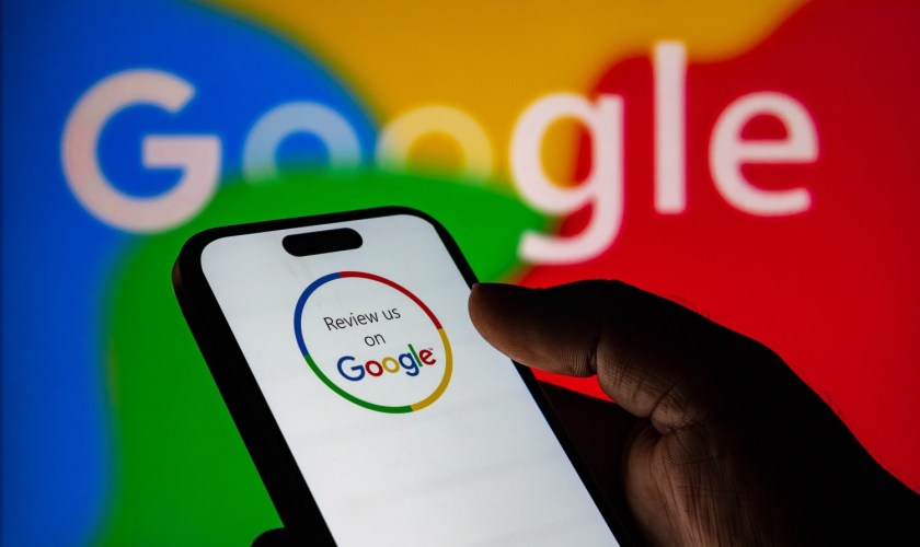 Closeup of a person holding a smartphone displaying a review us on google logo against a colorful background
