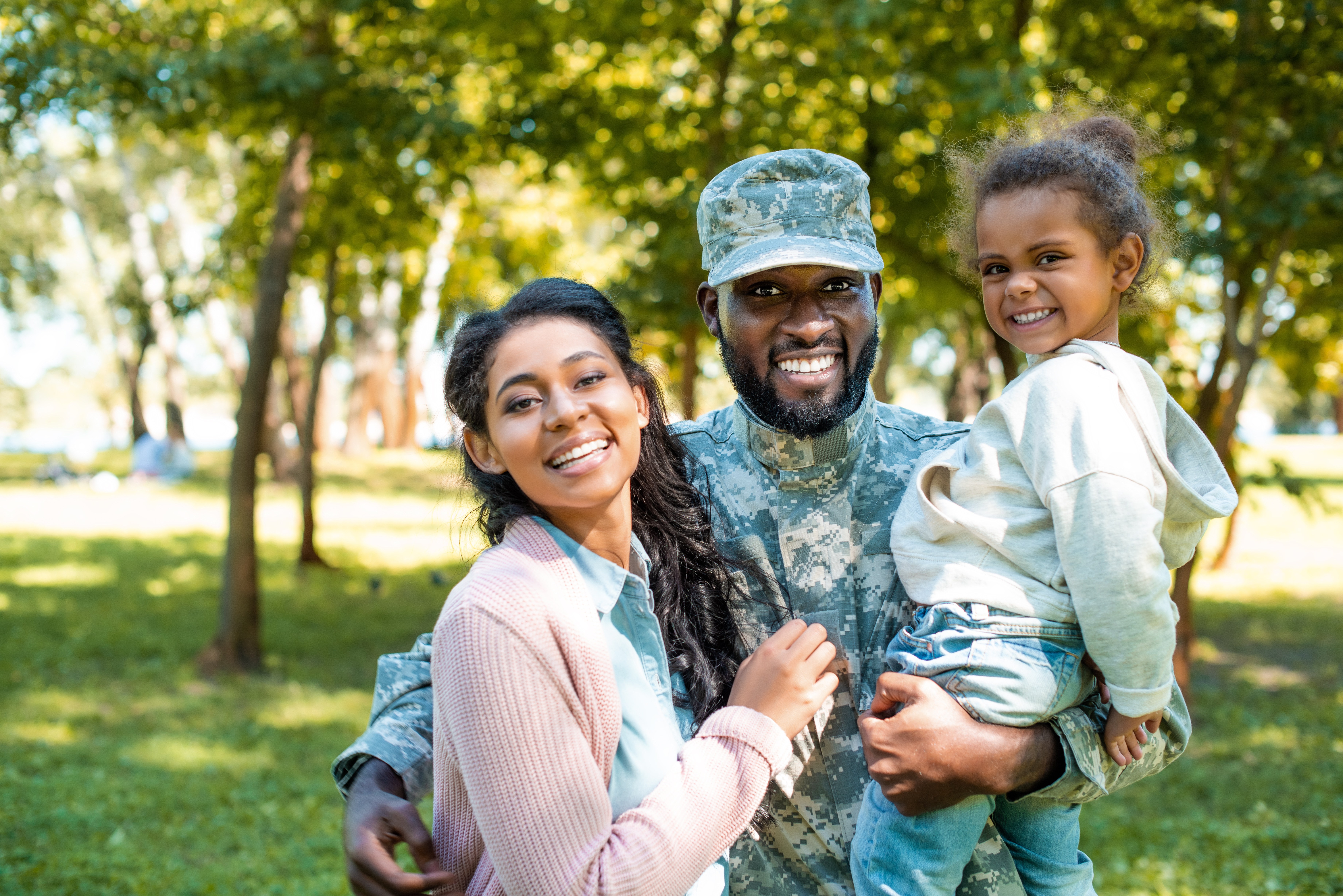 American soldier in military uniform looking at camera with family in park