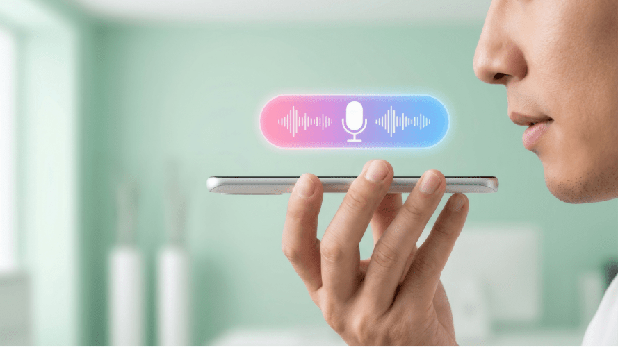 A person holding a smartphone with a voice assistant interface on the screen, featuring a microphone icon and colored sound waves. The background is a softly focused indoor setting with muted green tones.