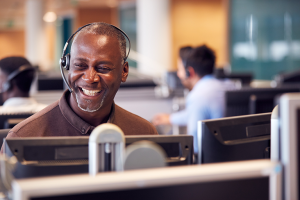 Homem sorrindo, sentado em frente ao computador, realizando uma chamada com o cliente.