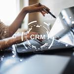 Ilustrações gráficas representando uma estratégia de CRM se sobrepõem à imagem de uma mulher utilizando um notebook.