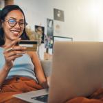 Mulher navega em notebook enquanto segura um cartão de crédito.