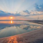 campo aberto, lago no meio e ao fundo engrenagens para gerar energia do vento