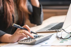 mulher fazendo cálculos segurando uma caneta e uma calculadora