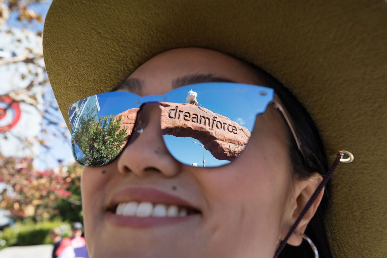 Entrada do Dreamforce reflete em óculos de mulher sorrindo.