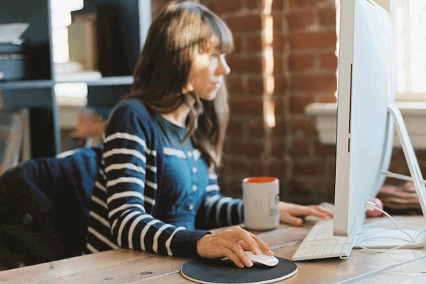 Frau im gestreiften Shirt sitzt am Rechner und guckt in ihn mit der Hand an der Maus