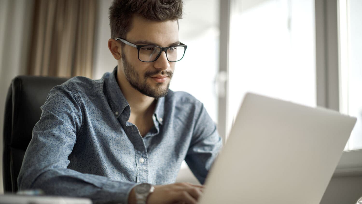 Jeune homme portant des lunettes et travaillant sur un ordinateur portable