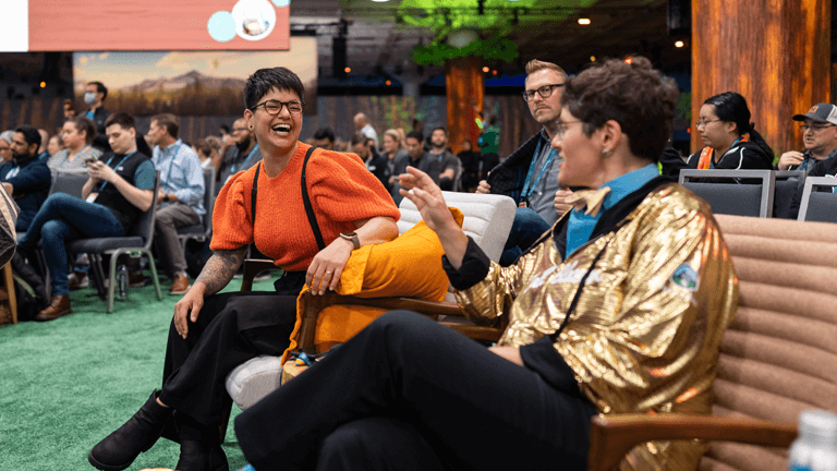 Trailblazer wearing a gold hoodie, sitting on a bench, chatting and laughing with another attendee