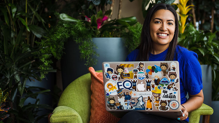 Woman sitting on a chair with an open laptop displaying many Salesforce stickers