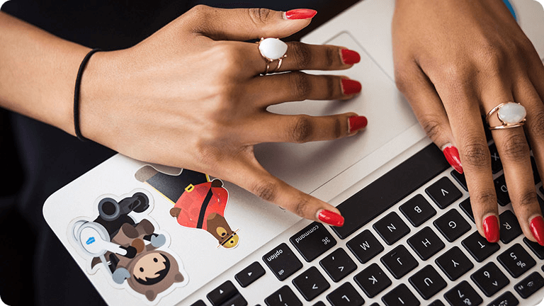 Closeup of a woman's hands working on a laptop with Salesforce stickers of Astro and Codey