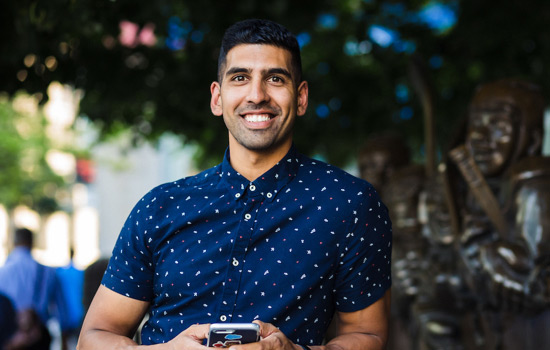 Omar Hussain from the finance team smiling and holding his phone