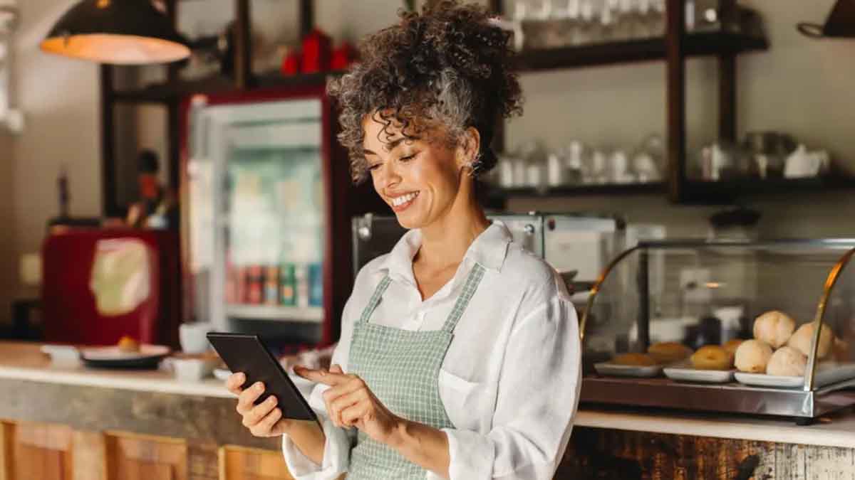 Woman standing in a restaurant, wearing an apron, using a tablet