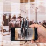 Eine Person hält ein Smartphone in der Hand und im Hintergrund ist ein Geschäft zu sehen. Die Grenzen zwischen Offline und Offline Handel verbinden sich.
