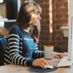 Frau im gestreiften Shirt sitzt am Rechner und guckt in ihn mit der Hand an der Maus