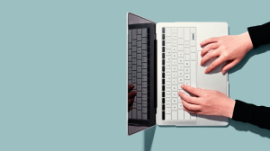 Auf einem türkisfarbenen Hintergrund steht ein Laptop, auf dem zwei Hände schreiben