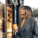 Eine Frau steht vor einem Schaufenster mit einem To-Go-Becher in der Hand