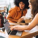 Zwei Frauen, die in einem Konsumgüterunternehmen an einem Laptop mit KI arbeiten.