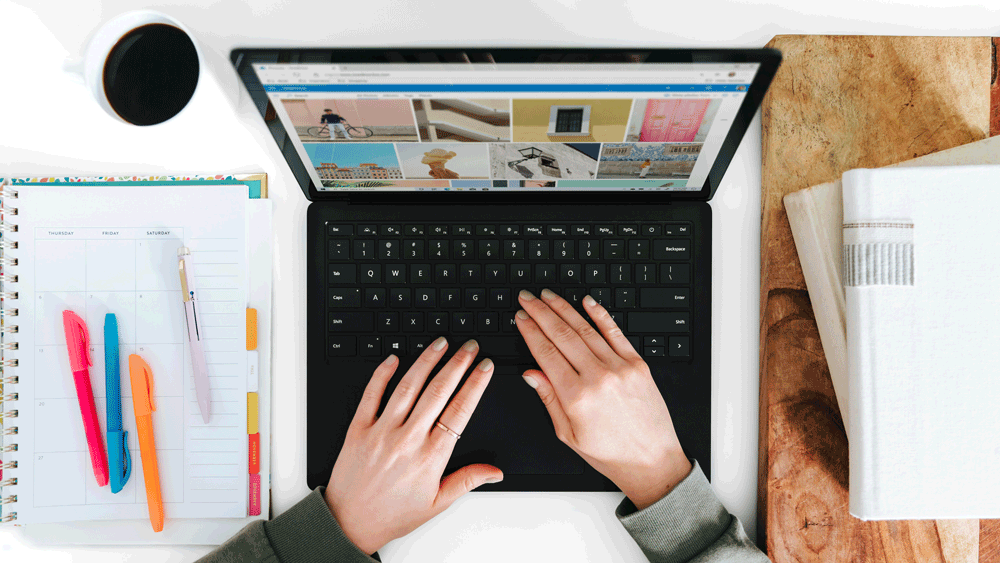 eine Person sitzt am Laptop und man schaut von oben auf den Schreibtisch