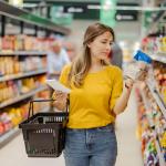 A woman reads the label of a food package in the aisle of a grocery store, a common consumer behavior.