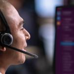Un hombre con auriculares habla delante de un monitor en el que se ve Slack en el fondo.