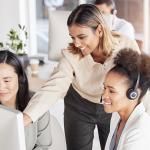 Three professionally dressed women review customer service operations on a computer.