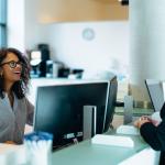 Woman behind a desk talks with another woman in an office setting / increase trust in government services