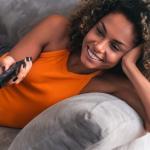 woman laying on couch with TV remote in her hand: subscription management