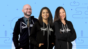 A group of three Developer Trailblazers stand together in their black Trailblazer hoodies against a blue background with line art details.
