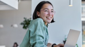 A young lady looking happy behind a laptop computer.