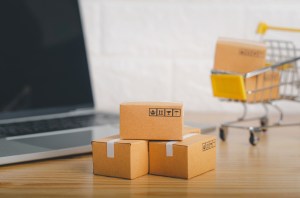 Brown paper boxs and cart with laptop on wood table in office background.Easy shopping with finger tips for consumers.Online shopping and delivery service concept