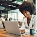 A smiling young Black woman uses her laptop to get self-service customer service in a cafe