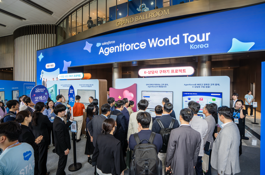 코엑스 그랜드볼룸에서 열린 Salesforce Agentforce World Tour Korea 컨퍼런스의 북적이는 부스 전경과 안내 스크린을 살펴보는 사람들