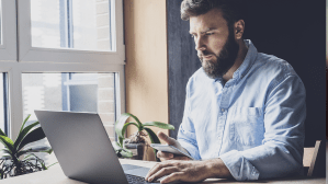 Man working by window in office using wireless digital gadgets for projects.