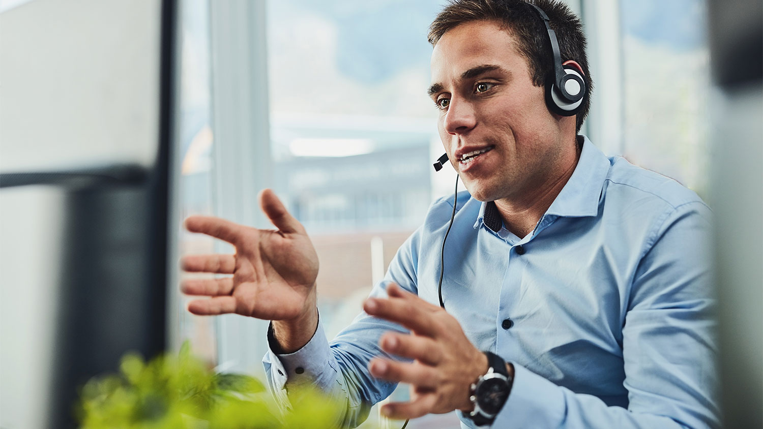A male contact center agent in a headset and blue collared shirt uses a case management system to deliver excellent service