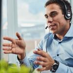 A male contact center agent in a headset and blue collared shirt uses a case management system to deliver excellent service