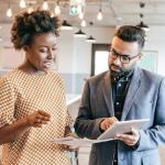 Photo of a man (holding a tablet) and a woman speaking in an office setting. / AI in B2B marketing