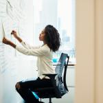 A woman entrepreneur sitting in a chair at a whiteboard arranging a project management system